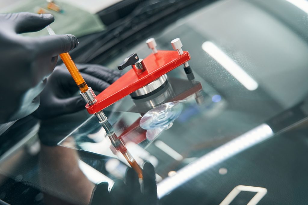 Serviceman in workshop fixing broken car window with vacuum filler